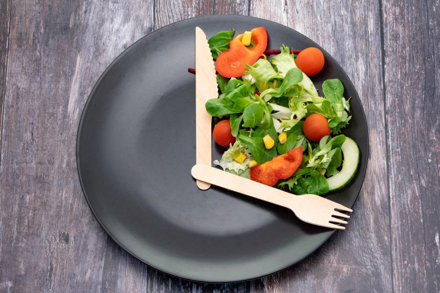A minimalist table setting with an empty plate and clock, representing cellular autophagy pathways during intermittent fasting.