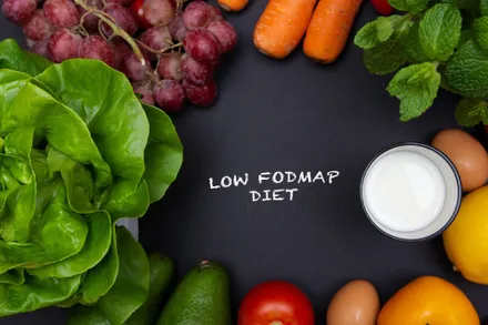 A clean low-FODMAP food table featuring fresh cucumbers, carrots, chicken breast, white rice, extra virgin olive oil, and kiwi fruit.