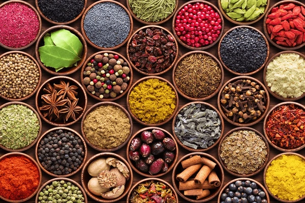 A colorful array of traditional Indian spices including golden turmeric powder, black pepper, cardamom pods, and cinnamon bark.