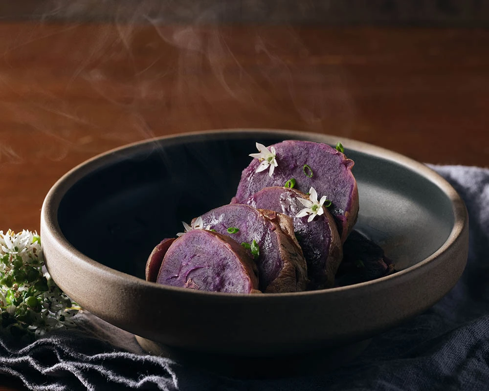 Steamed Okinawan purple sweet potatoes sliced open to reveal deep violet flesh rich in anthocyanin antioxidants.