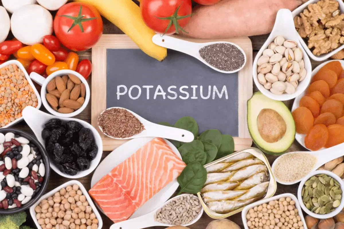 A vibrant arrangement of potassium-dense whole foods including baked sweet potatoes, avocados, spinach, and coconut water.